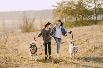 Canva - Female friends in face masks walking with dogs in countryside